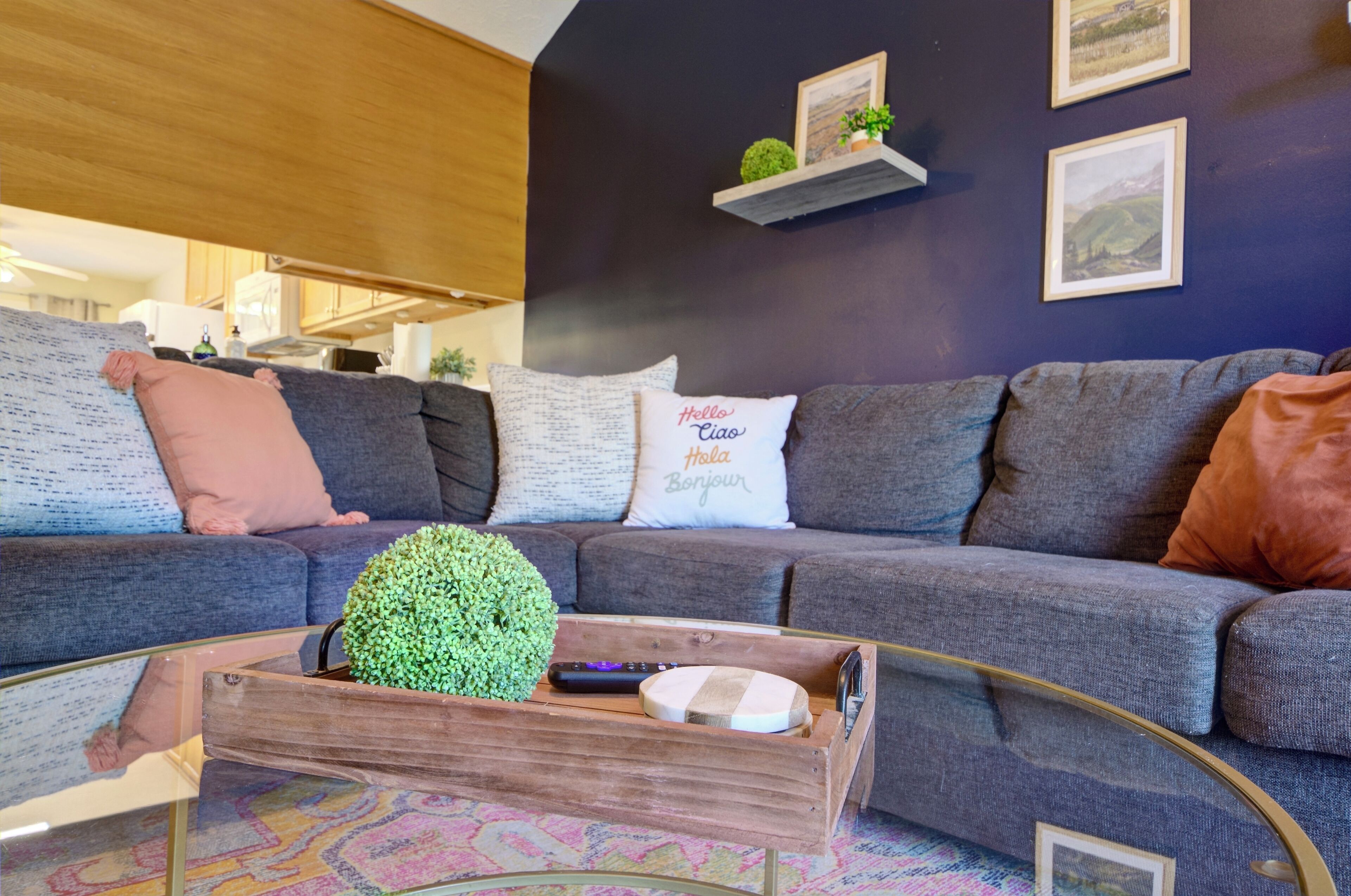 A living room with a grey sofa, a glass coffee table, and a wooden side table with a green plant.
