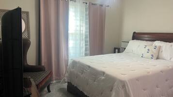 A bedroom with a bed, a chair, a nightstand, a ceiling fan, and a window with curtains.