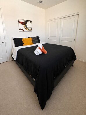 Une chambre avec une couvre-lit noire, des oreillers blancs et noirs, un plaid jaune et une serviette blanche.