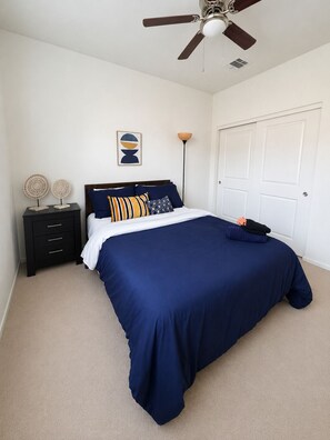 A bedroom with a bed, a nightstand, a ceiling fan, a door, and a wall-mounted lamp.
