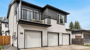 Een huis met twee verdiepingen, een balkon, drie garagepoorten en een houten omheining.