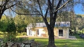 A house with a stone wall, a bench, and a tree in front.
