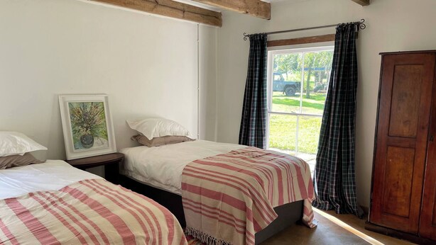 A bedroom with two beds, a window with curtains, a wooden wardrobe, and a framed picture on the wall.