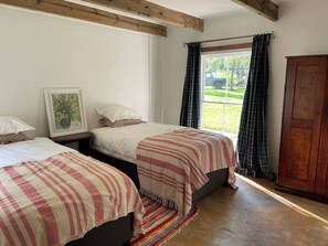 A bedroom with two beds, a window with curtains, a wooden wardrobe, and a framed picture on the wall.