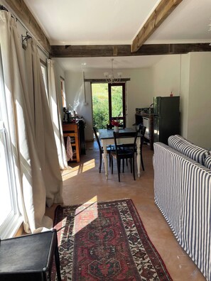 Una habitación con una mesa de comedor, sillas, un sofá, un tapete y una zona de cocina con refrigerador.