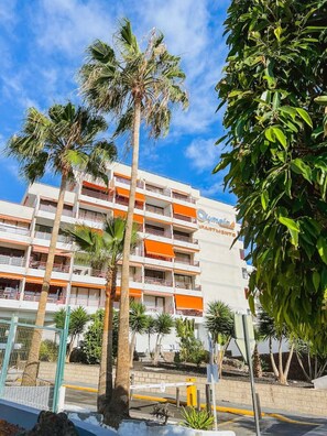 Ein mehrstöckiges Hotel mit Balkonen, Palmen und blauem Himmel.