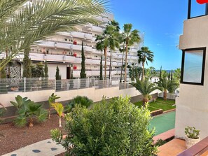 Ein mehrstöckiges Hotel mit Balkonen, Palmen und einem Schwimmbecken.