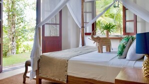 A bedroom with a bed, a nightstand, a decorative elephant, a window with a view of greenery, and a door.