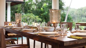 A wooden dining table set with plates, glasses, and a candle holder, surrounded by chairs.