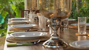 Een gedekte tafel met borden, glazen en een zilveren middelpunt, omringd door geweven placemats.