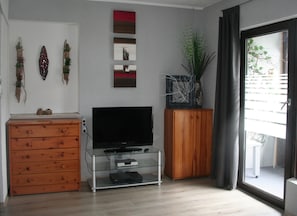 A living room with a TV on a glass stand, wooden cabinets, and wall art. - Vacation apartment Hexenhäusla Peace and relaxation in the heart of Franconian Switzerland (Gößweinstein)