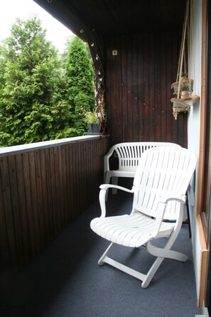 A balcony with a white chair, a wooden wall, and a hanging plant. - Vacation apartment Hexenhäusla Peace and relaxation in the heart of Franconian Switzerland (Gößweinstein)
