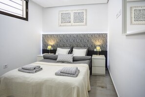 A bedroom with a bed, two bedside tables, a headboard, and wall-mounted decorative panels. - Luxury Summerland: Stylish 1BR Retreat in Los Cristianos with Pool & Terrace (Los Cristianos)