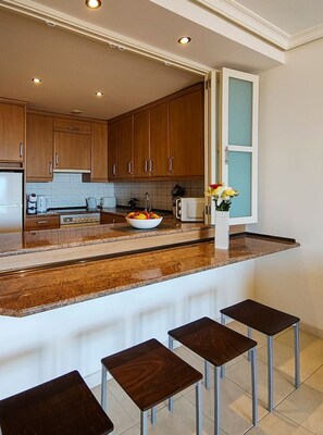 Eine moderne Küche mit Holzausstattung, einer Granit Arbeitsplatte, einer Obstschale, einer Mikrowelle und einem Fenster mit Aussicht.