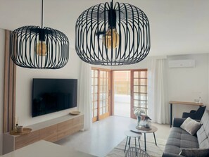 Ein modernes Wohnzimmer mit einem Flachbildfernseher, einer Couch, einem Couchtisch und zwei schwarzen Pendelleuchten.
