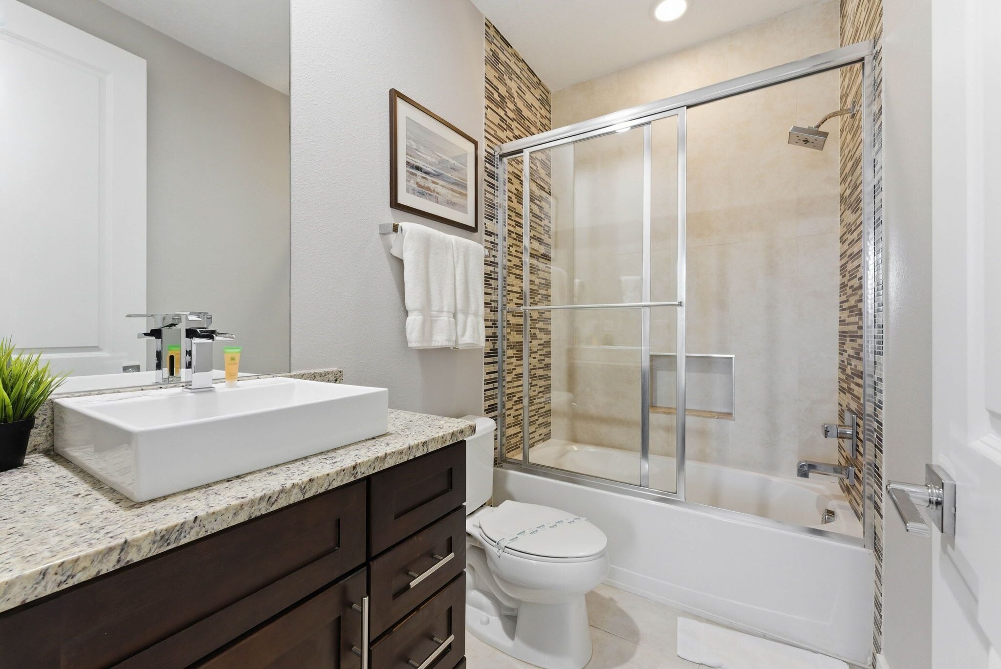 A bathroom with a white sink, dark wooden cabinets, a toilet, and a glass-enclosed shower.