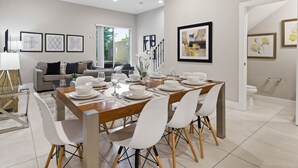 A modern dining area with a wooden table set for four, white chairs, and framed artwork on the walls. - Family Retreat With 4bed Suites & Private Jacuzzi (Kissimmee)