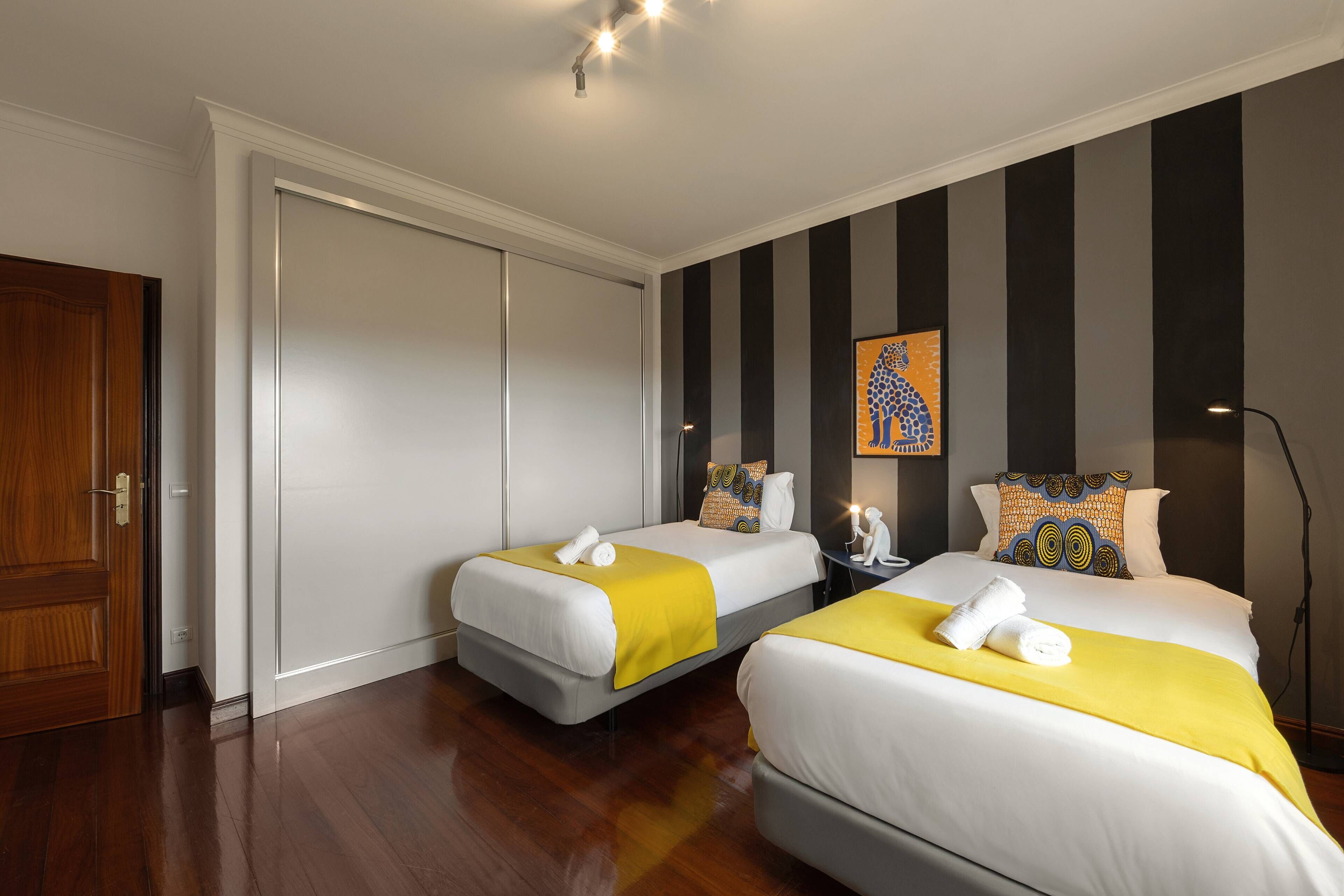 A hotel room with two beds, a wardrobe, a painting, and a lamp.