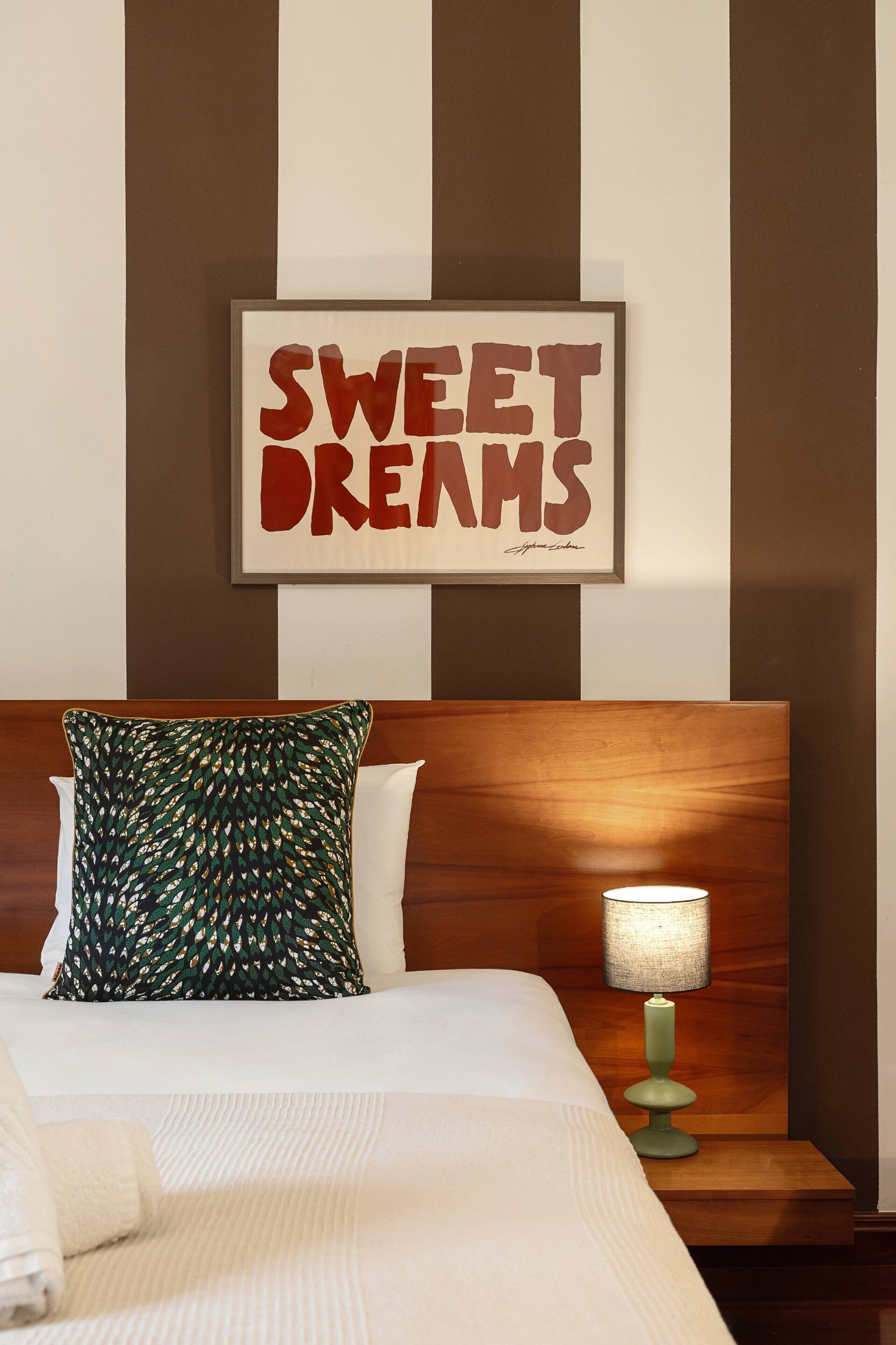 A neatly made bed with a pillow, a bedside lamp, and a framed sign on the wall.