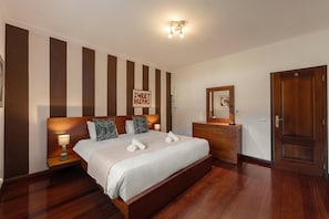 Ein Hotelzimmer mit einem großen Bett, einem Nachttisch mit Lampe, einem Schminktisch, einem Spiegel und einer Tür.