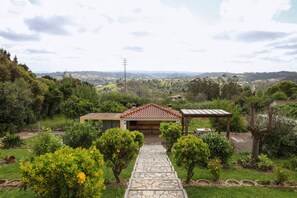 Ein Haus mit einem Kiesweg, der zu einer Garage führt, umgeben von üppiger Vegetation und Blick auf ferne Hügel.