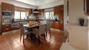 A modern kitchen with wooden cabinets, a dining table with chairs, and a large window. - Casa Favorita - Rustic Hideaway (Alcobaça)