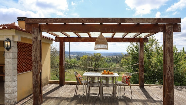 A wooden deck with a pergola, a table with chairs, and a hanging light fixture. - Casa Favorita - Rustic Hideaway (Alcobaça)