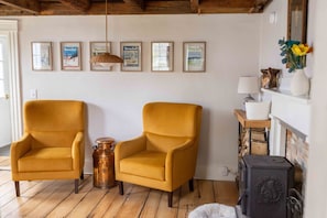 Una habitació amb dues butaques de color mostassa, una olla de coure, una llar de foc i quadres emmarcats a la paret.