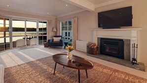 A spacious living room with a fireplace, a television mounted above it, and a view of a lake through large sliding glass doors.