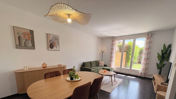 En moderne stue med spiseplads, sofa og et stort vindue med gardiner.