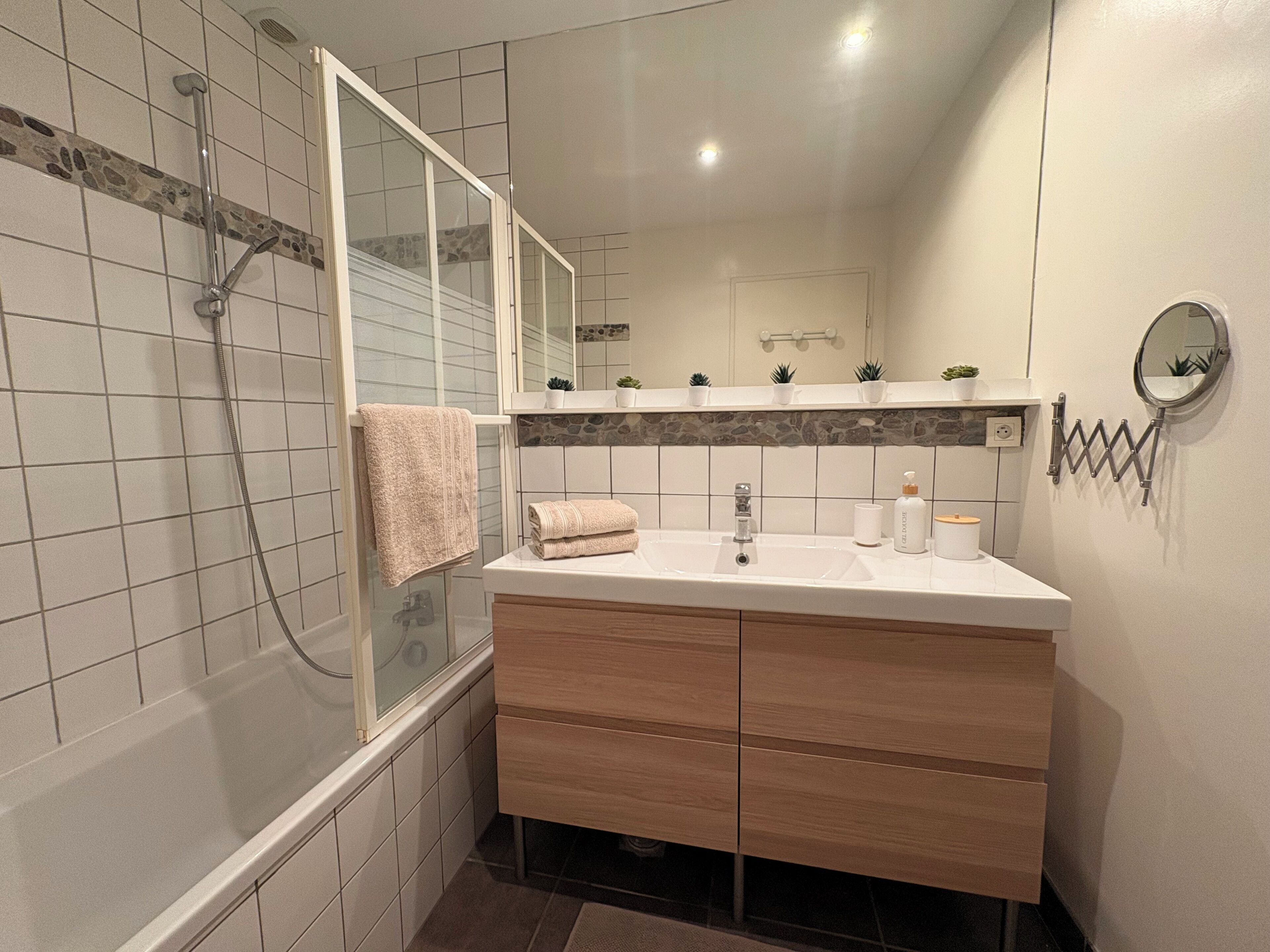Une salle de bain moderne avec une douche à parois de verre, un meuble-lavabo avec miroir et un sol carrelé.