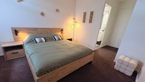 Et soveværelse med en træseng, sengeborde, et natbord, en lampe monteret på væggen og en dør til et badeværelse.