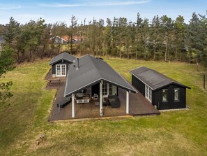Ein zweistöckiges Haus mit einer Terrasse, umgeben von einem bewaldeten Gebiet.