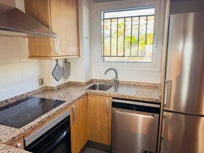 A kitchen with a built-in stove, dishwasher, stainless steel refrigerator, and a window with a view of greenery. - Casa Heidi - Pool, Garage & Terrace - Puerto de Santiago (Santiago del Teide)