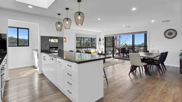 Una cocina moderna con una isla central, armarios blancos e iluminación colgante.