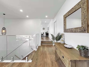 A modern interior with a staircase, wooden flooring, a glass railing, a wooden console table, and a decorative wall piece.