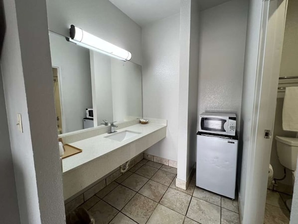 A bathroom with a sink, mirror, and a refrigerator.