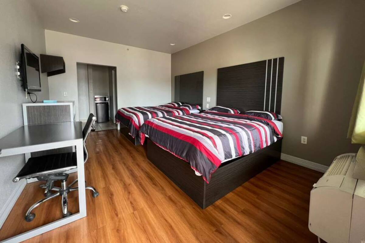 A modern bedroom with a large bed, a desk, a chair, a television, and a built-in wardrobe.
