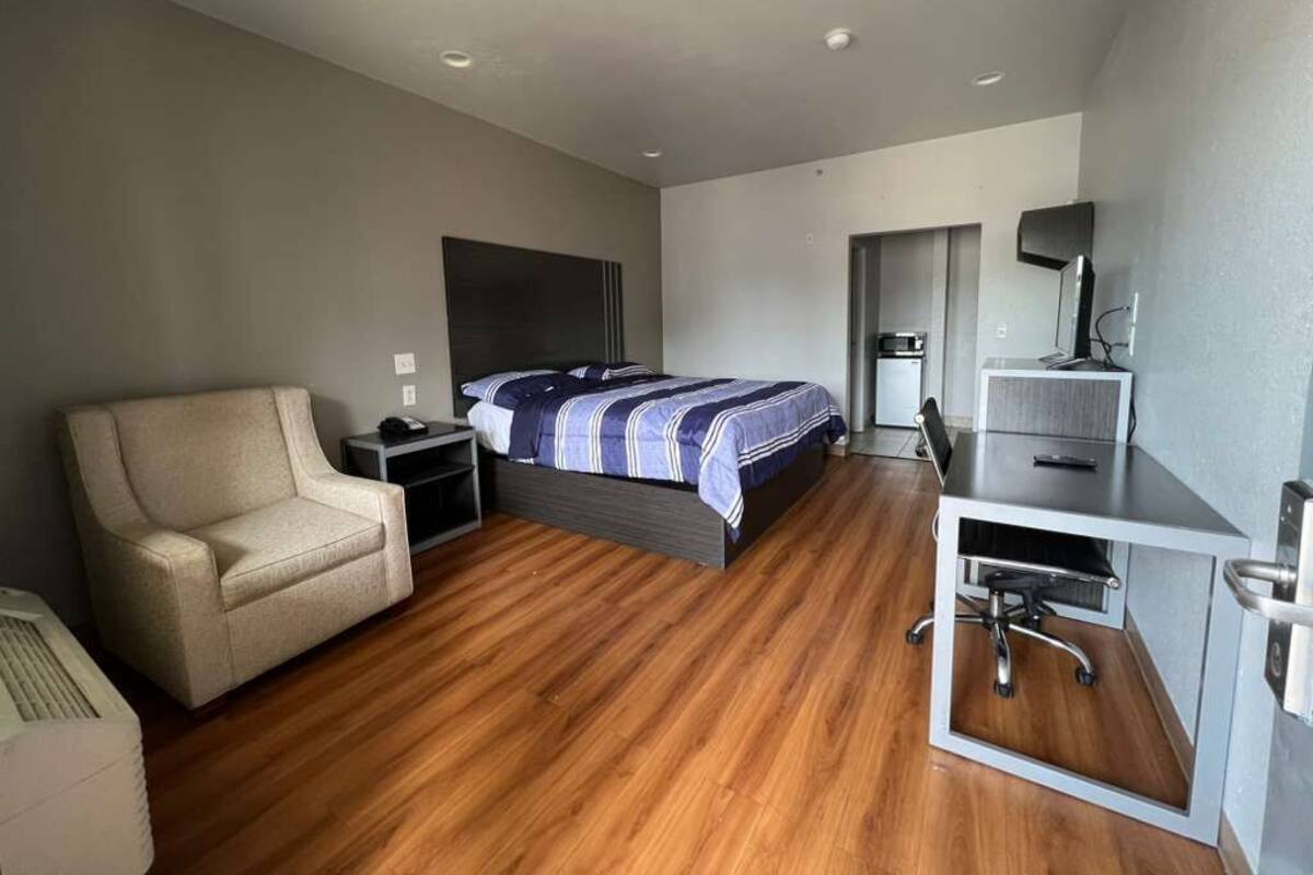 A modern hotel room with a bed, a desk, a chair, a sofa, and a TV.