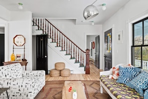 Una sala de estar con una escalera, un sofá, un diván estampado y un ventanal grande.