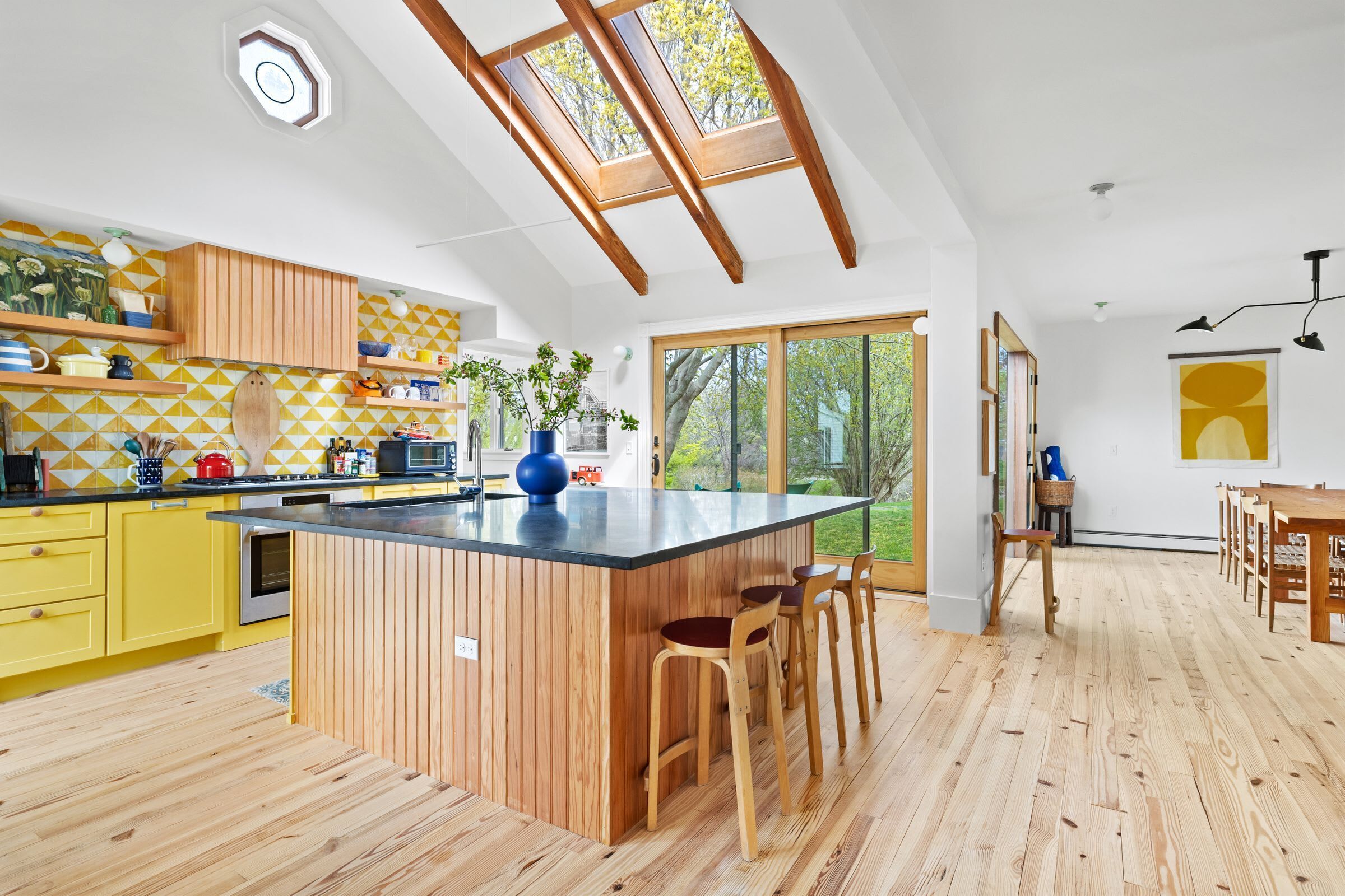 A modern kitchen with a central island, wooden flooring, and a skylight.