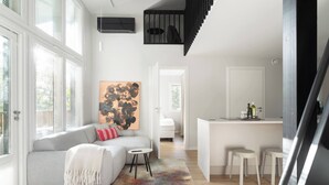 Una sala de estar moderna con un sofá gris, un tapete colorido, un cuadro abstracto grande y una escalera que lleva a una zona de cocina con taburetes.