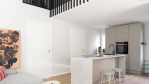 Una cocina moderna con una isla central, una zona de comedor con taburetes y un espacio de sala con sofá y un cuadro.