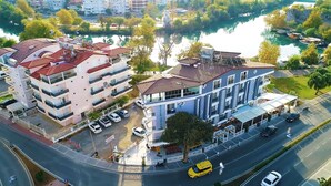 A multi-story hotel with balconies, a riverside view, and a parking area. - River Suite Otel (Manavgat)