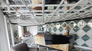 A modern interior with a checkered floor, grey sofas, a wooden coffee table, and a reception desk with a patterned wall. - River Suite Otel (Manavgat)