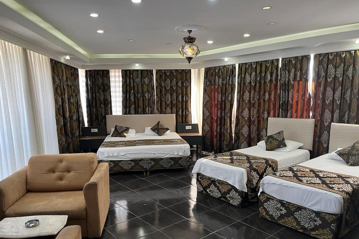 A hotel room with two beds, a sofa, a table, and a chandelier.