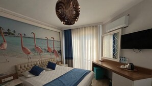 A hotel room with a bed, a desk, a television, and a painting of flamingos. - River Suite Otel (Manavgat)