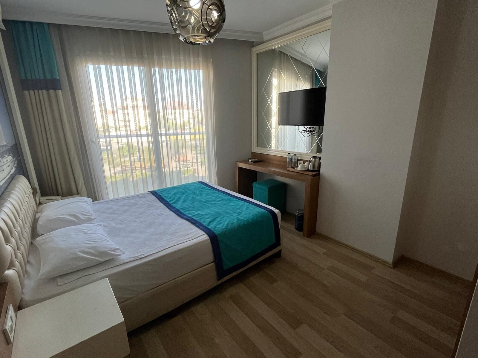 Una camera d'albergo con un letto, una scrivania, una televisione e una finestra con tende.