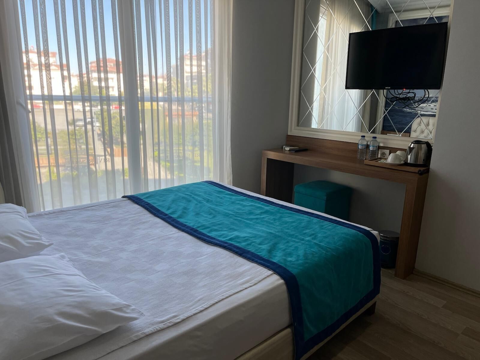 A hotel room with a bed, a desk, a television, and a window with blinds.