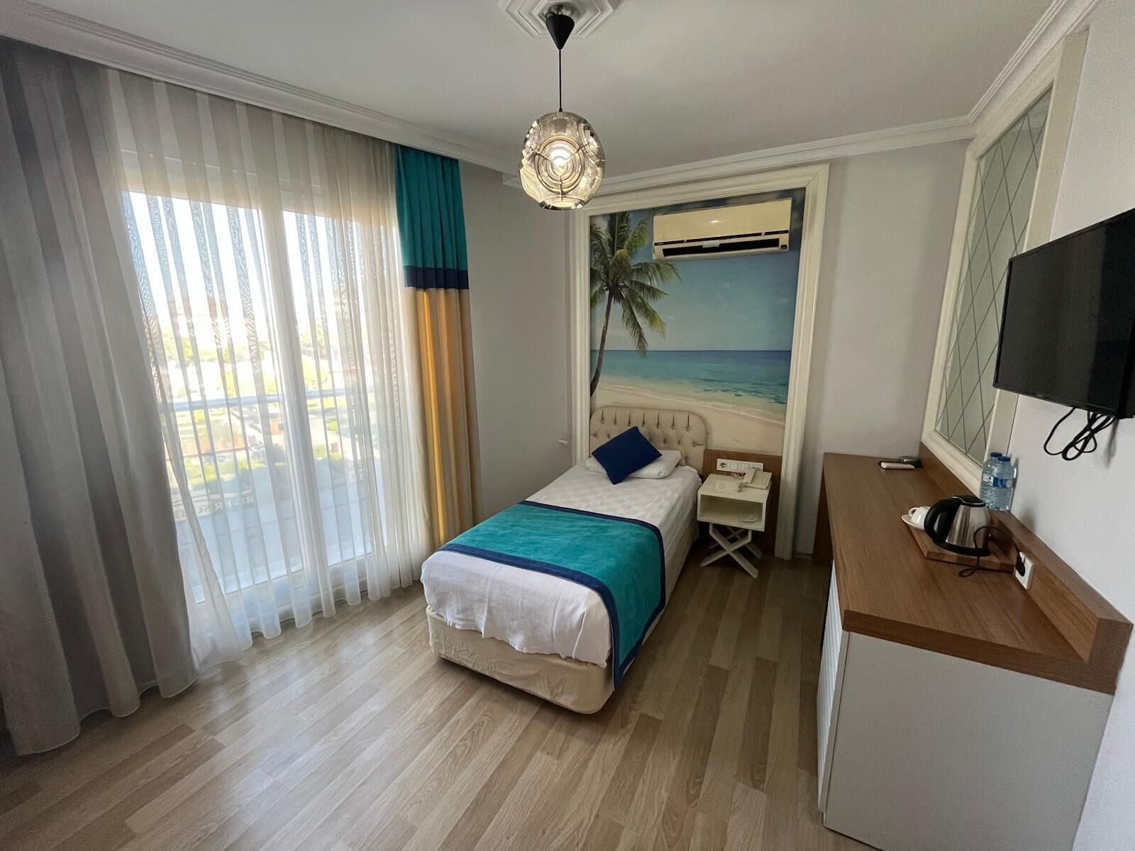 A hotel room with a bed, a desk, a TV, and a view of the beach.